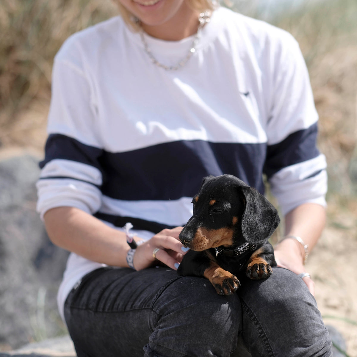 Ellie Wales wearing an original Whale Of A Time Clothing design with a young dachshund puppy on her lap at the beach